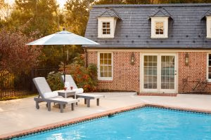 Two poly chaise lounges with side table and umbrella beside pool
