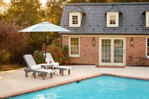Two poly chaise lounges with side table and umbrella beside pool