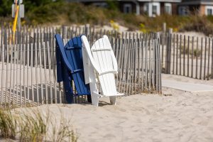 Poly Adirondack chairs folded and set against a picket fence on the beach.