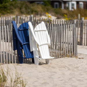 Poly Adirondack chairs folded and set against a picket fence on the beach.