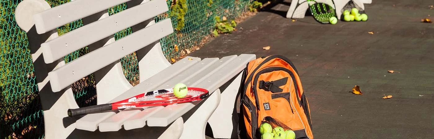 Park bench on tennis court with tennis raquet and balls lying around