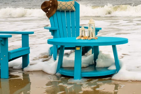 finch poly adirondack chairs and table on beach with the surf washing around the chairs.