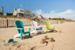 Three different colored poly chairs sitting on the beach with a small sand castle in front.