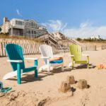 Three different colored poly chairs sitting on the beach with a small sand castle in front.