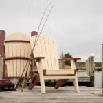 Two polly chairs sitting on the dock with fishing rods propped up against the chairs.