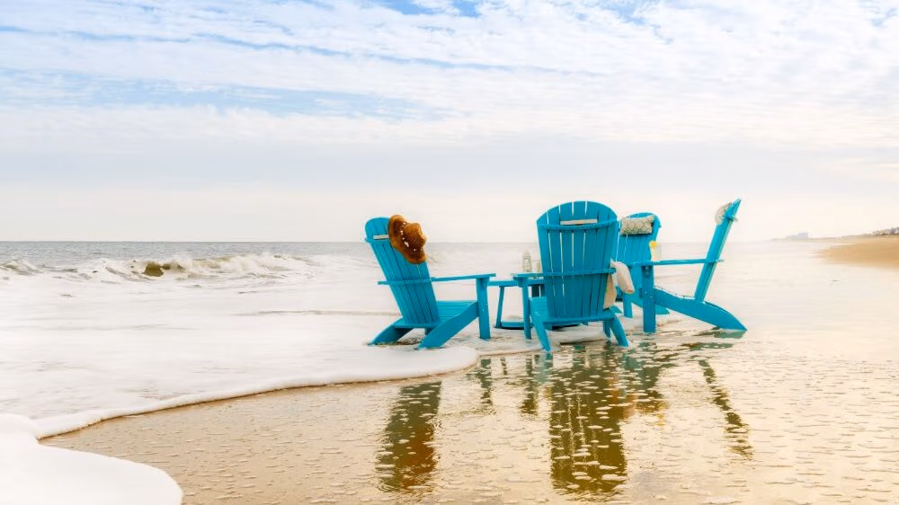 4 aqua poly chairs sitting around a center table on the beach. 