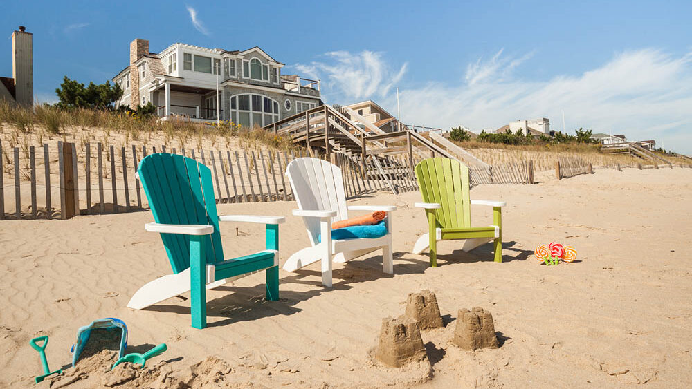 Three different colored poly chairs sitting on the beach with a small sand castle in front. 