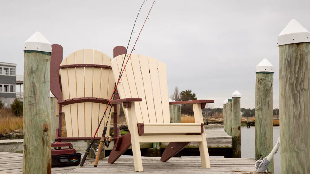 Two polly chairs sitting on the dock with fishing rods propped up against the chairs. 