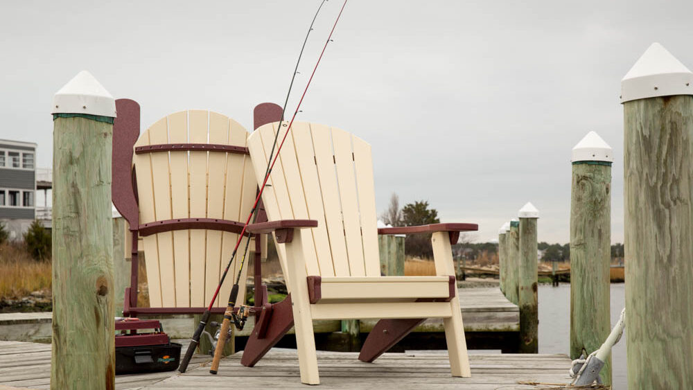 Two polly chairs sitting on the dock with fishing rods propped up against the chairs. 